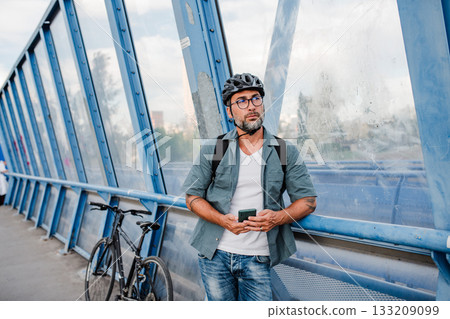 Bearded cyclist using phone while waiting for bus. 133209099