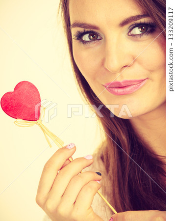 Flirty woman holding red wooden heart on stick Flirty woman holding red wooden heart on stick 133209117