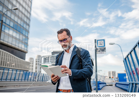 Mature man reading while waiting for bus. Mature man reading while waiting for bus. 133209149