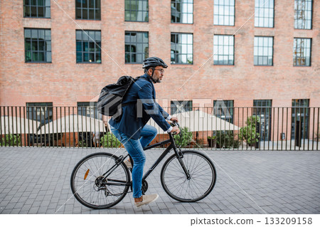 Side view of businessman riding bike to office, wearing backpack and helmet. Side view of businessman riding bike to office, wearing backpack and helmet. 133209158