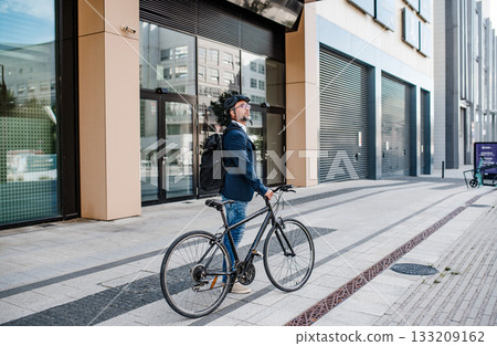 Side view of businessman riding bike to office, wearing backpack and helmet. 133209162