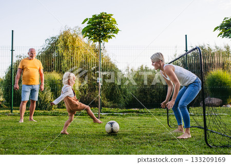 Little boy playing football with mother and grandfather in backyard. 133209169