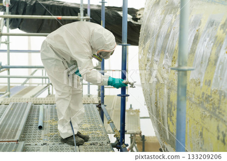 Worker in protective suit completes maintenance on aircraft fuselage during restoration at an aerospace facility in a controlled environment 133209206