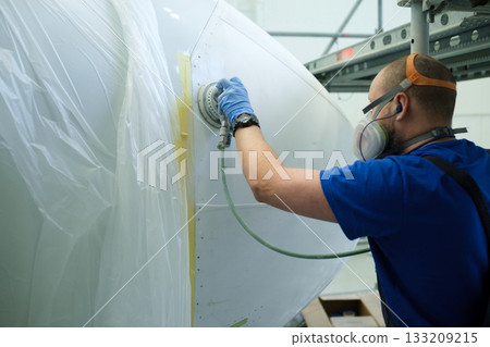 Technician performing surface preparation on an aircraft component in a well-lit workshop environment during daytime 133209215