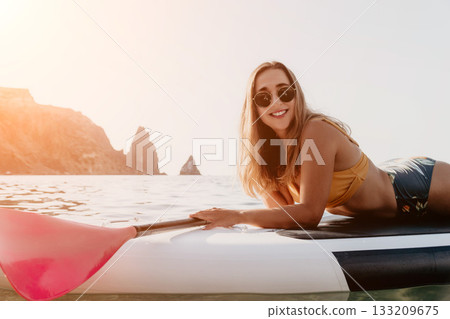 Woman Paddleboarding Ocean Coastline - Smiling woman on paddleboard enjoying summer day on the ocean with mountains in the background. 133209675