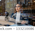 Thoughtful woman enjoying coffee in a cafe with city reflections. A woman sits at a table in a cafe, her hand gently holding a cup of coffee.  133210086
