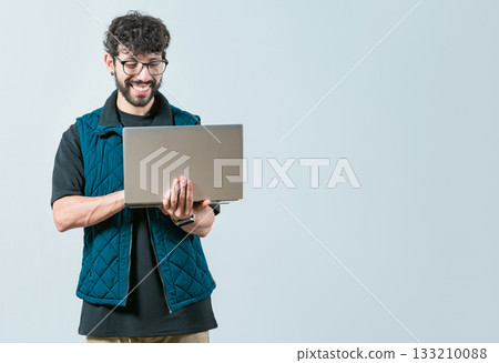 Handsome young man with glasses holding and looking on laptop screen. Portrait of Bearded guy using and looking laptop isolated Handsome young man with glasses holding and looking on laptop screen. Portrait of Bearded guy using and looking laptop isolated 133210088