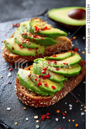 A spread of whole-grain toast topped with fresh avocado slices and a sprinkle of chili flakes, for a healthy snack. 133210184