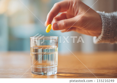 A close-up of a hand dropping a vitamin pill into a glass of water, symbolizing daily wellness routine. A close-up of a hand dropping a vitamin pill into a glass of water, symbolizing daily wellness routine. 133210249
