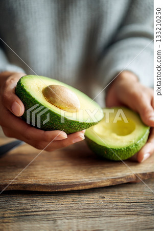 A close-up of a person's hands slicing a ripe avocado, revealing its creamy green interior, perfect for healthy fats. 133210250