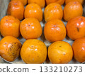 A pile of ripe juicy orange persimmons in a box, on sale at a supermarket vegetable stand, showcases organic, vegetarian and healthy food. Close-up. 133210273