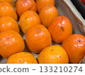 A pile of ripe juicy orange persimmons in a box, on sale at a supermarket vegetable stand, showcases organic, vegetarian and healthy food. Close-up. 133210274