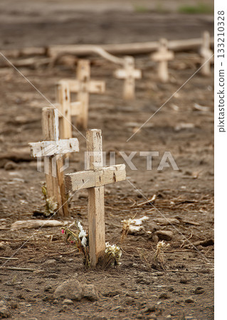 Makeshift graves marked by simple wooden crosses on barren land, a somber reminder of widespread loss and tragedy. 133210328