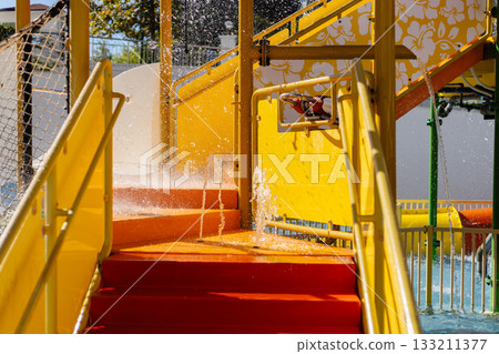 Children enjoy a thrilling day at a vibrant water park, splashing through bright yellow slides and steps. Laughter fills the air as water cascades down, creating a joyful atmosphere Children enjoy a thrilling day at a vibrant water park, splashing through bright yellow slides and steps. Laughter fills the air as water cascades down, creating a joyful atmosphere 133211377