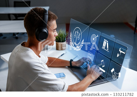 Young man using laptop with headphones while exploring legal icons on a screen Young man using laptop with headphones while exploring legal icons on a screen 133211782
