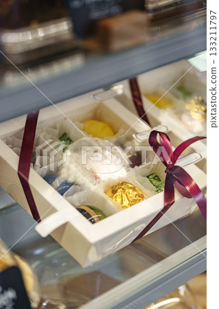 Colorful dessert gift box with a ribbon displayed in a dessert shop showcase Colorful dessert gift box with a ribbon displayed in a dessert shop showcase 133211797