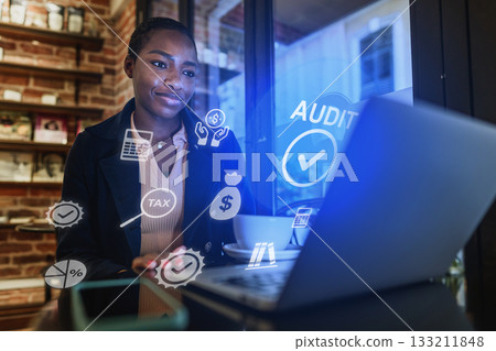 Young professional working on laptop with financial icons in a cozy cafe setting Young professional working on laptop with financial icons in a cozy cafe setting 133211848