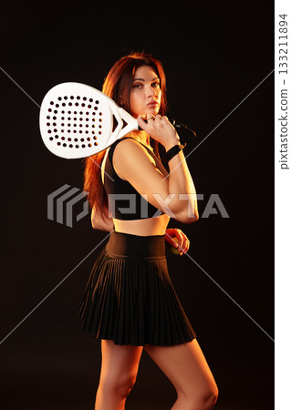 Young woman poses confidently with a large racquet in a studio setting 133211894