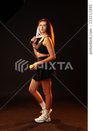 Female tennis player poses confidently with racket and tennis ball in studio setting 133211895