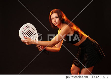 Young woman prepares to play paddle tennis in a stylish sports outfit indoors 133211897