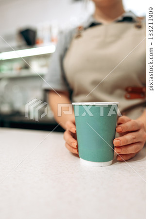 Barista serving coffee in a cafe with green cup on a countertop near afternoon light 133211909