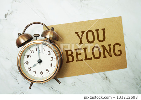 You Belong text written on paper card with alarm clock on marble background 133212698