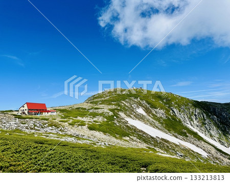 A red-roofed mountain hut against the blue sky and a summer Alps landscape A red-roofed mountain hut against the blue sky and a summer Alps landscape 133213813