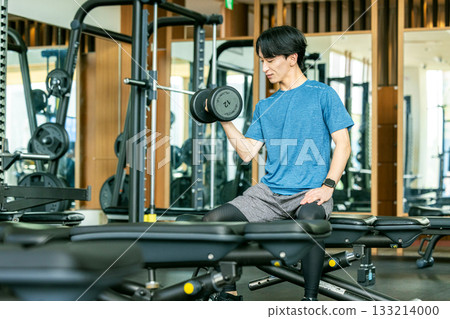 A young man doing muscle training with dumbbells at a training gym A young man doing muscle training with dumbbells at a training gym 133214000