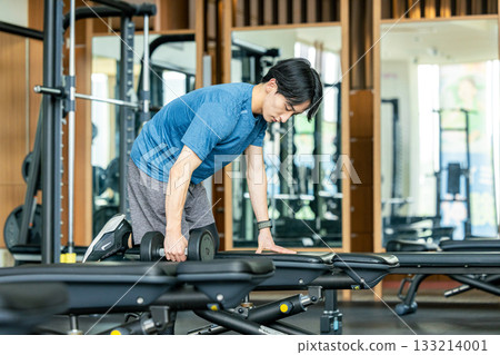 A young man doing muscle training with dumbbells at a training gym 133214001