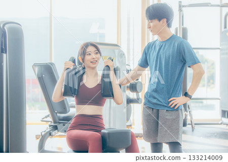 一位女士正在健身房跟隨教練進行肌力訓練。 133214009