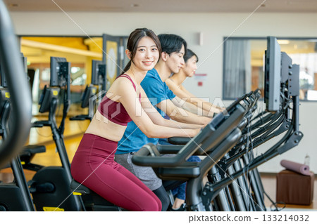 Men and women using upright bikes at the gym Men and women using upright bikes at the gym 133214032