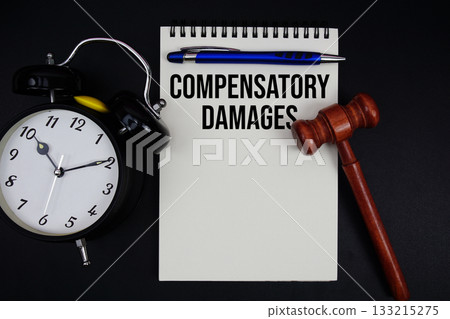 Compensatory Damages text written on notepad with gavel and alarm clock on black background 133215275