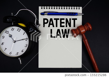 Patent Law text written on notepad with gavel and alarm clock on black background 133215286