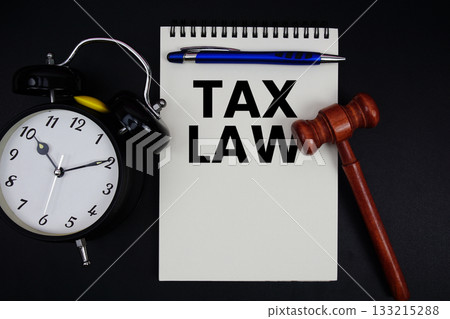 Tax law text written on notepad with gavel and alarm clock on black background 133215288