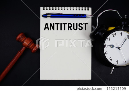 Antitrust text written on notepad with gavel and alarm clock on black background 133215309