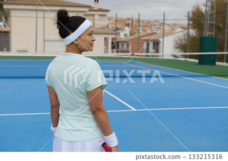 Woman On Blue Tennis Court Looking Over Shoulder With Headband And Racquet 133215316