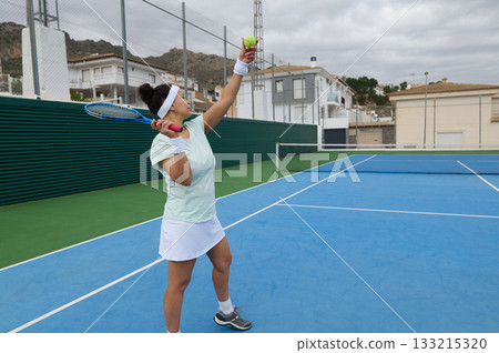Athlete Serves Tennis Ball on Outdoor Court, Focused Female Player in Action 133215320