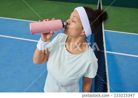 Athletic Woman Drinking Pink Smoothie On Tennis Court After Practice 133215347