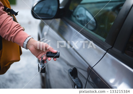 Person Holding Car Keys In Front Of a Silver Car Door, Ready To Drive 133215384