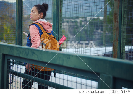 Woman With Orange Backpack On Bridge Carrying Pink Yoga Mat Looking Over City 133215389