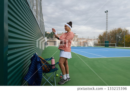 Athlete Woman Adjusting Wristband On Tennis Court By Wall 133215396