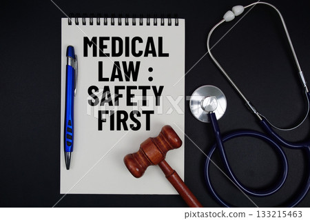 Notepad with "Medical Law: Safety First" a pen, gavel, and stethoscope on a black background 133215463