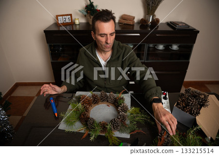 Man Creating Pinecone Wreath For Christmas Decor In Cozy Home Setting Man Creating Pinecone Wreath For Christmas Decor In Cozy Home Setting 133215514