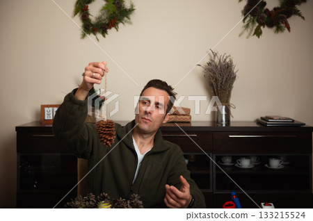 Man Hanging Pine Cone Ornament During Christmas Craft At Cozy Home Setting 133215524