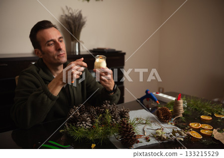 Man Crafting Christmas Decorations With Pinecones And Dried Citrus In Cozy Home Setting Man Crafting Christmas Decorations With Pinecones And Dried Citrus In Cozy Home Setting 133215529