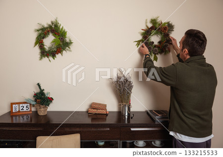 Man Hanging Christmas Wreaths At Home Office Decor Scene With Holiday Plants 133215533