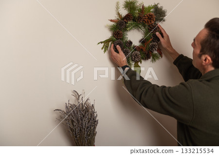 Man Hanging Christmas Wreath on Wall During Home Decor Project 133215534