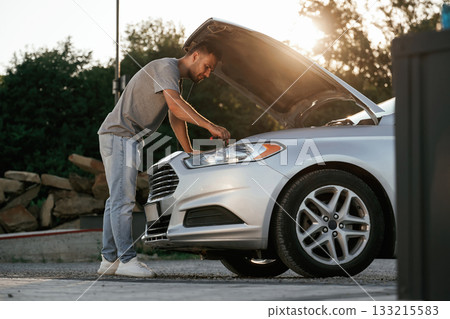 Beautiful sunlight. Hood is opened, guy is repairing the automobile. Man is with his car outdoors Beautiful sunlight. Hood is opened, guy is repairing the automobile. Man is with his car outdoors 133215583