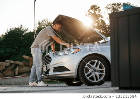 Beautiful sunlight. Hood is opened, guy is repairing the automobile. Man is with his car outdoors Beautiful sunlight. Hood is opened, guy is repairing the automobile. Man is with his car outdoors 133215584