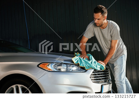 View from the side, using cloth to polish the automobile. Man is with his car outdoors View from the side, using cloth to polish the automobile. Man is with his car outdoors 133215727